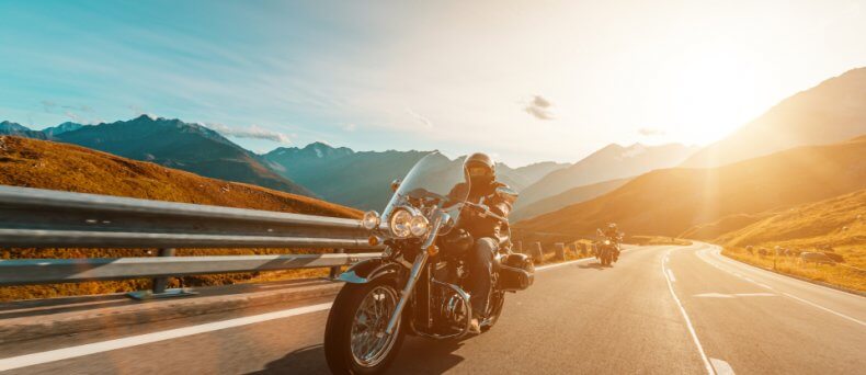 Side front view of two motorcycle riders on the road during sunset