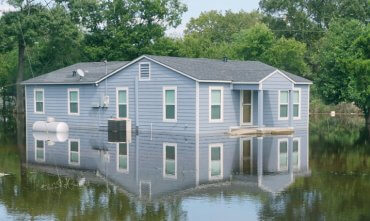 flooded home half submerged in water with trees in the background