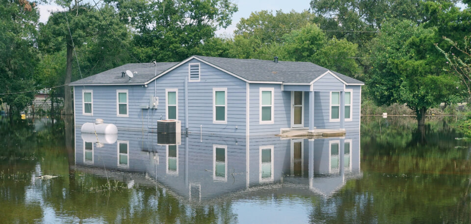 flooded home half submerged in water with trees in the background