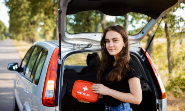 young woman standing behind car with first aid kit