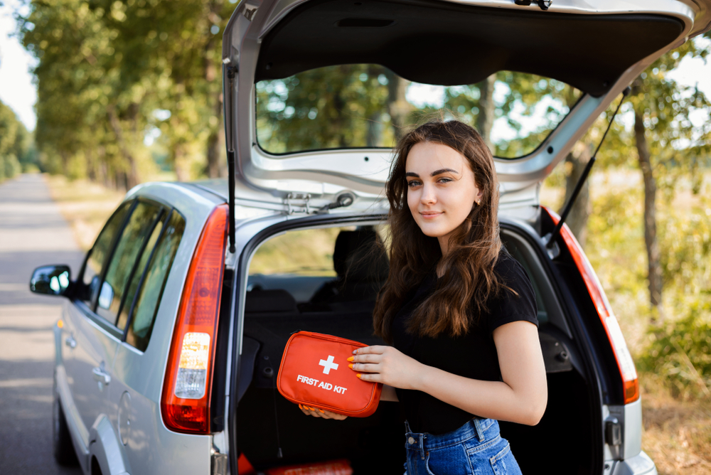 young woman standing behind car with first aid kit