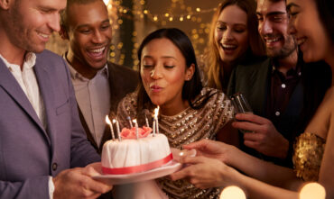 woman blowing out candles on birthday cake with friends surrounding her