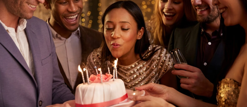 woman blowing out candles on birthday cake with friends surrounding her