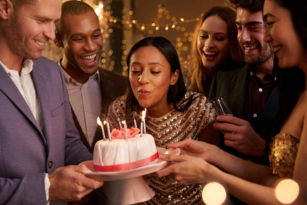 woman blowing out candles on birthday cake with friends surrounding her