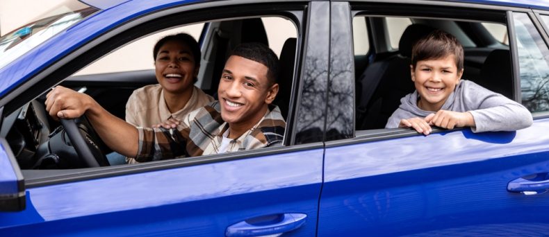 Cheerful parents and little son sitting in car together, happy spouses and male child looking out of window, ready for summer trip after they compared car insurance rates to find the lowest car insurance in Georgia.
