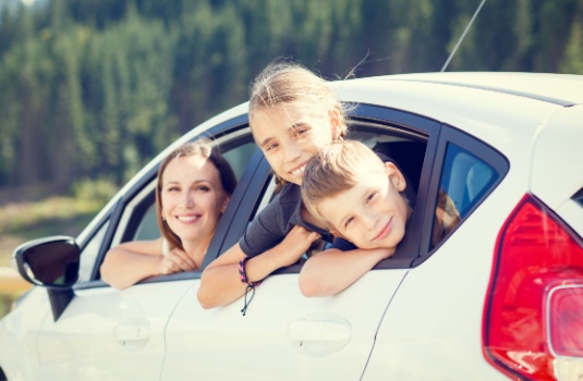 Happy young woman and her children sitting in a car and look out from windows after setting a goal to find the lowest car insurance in Georgia.