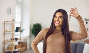 young woman holding up keys to first apartment