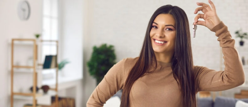 young woman holding up keys to first apartment