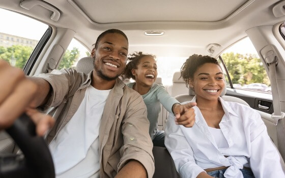 Friends smiling inside a car during a sunny drive, capturing a carefree road trip moment with comprehensive car insurance in Georgia.