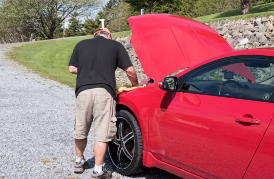 Man does vehicle maintenance on his car in the driveway to help his car last longer in Georgia.