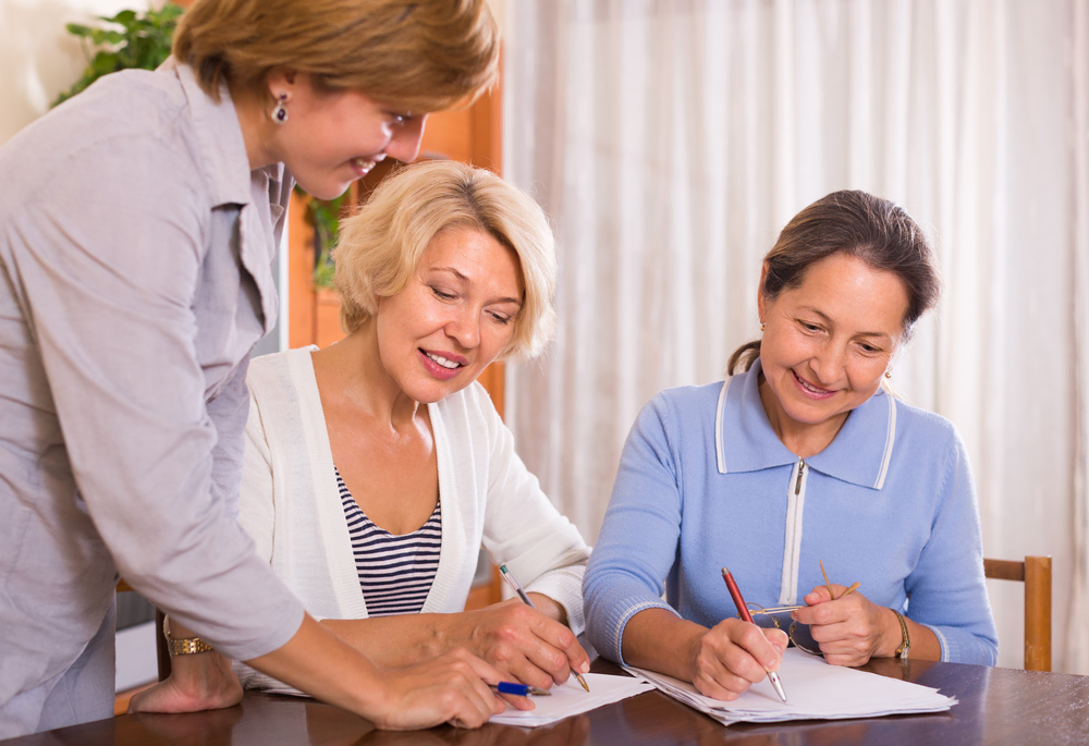 Two happy mature ladies sign life insurance documents