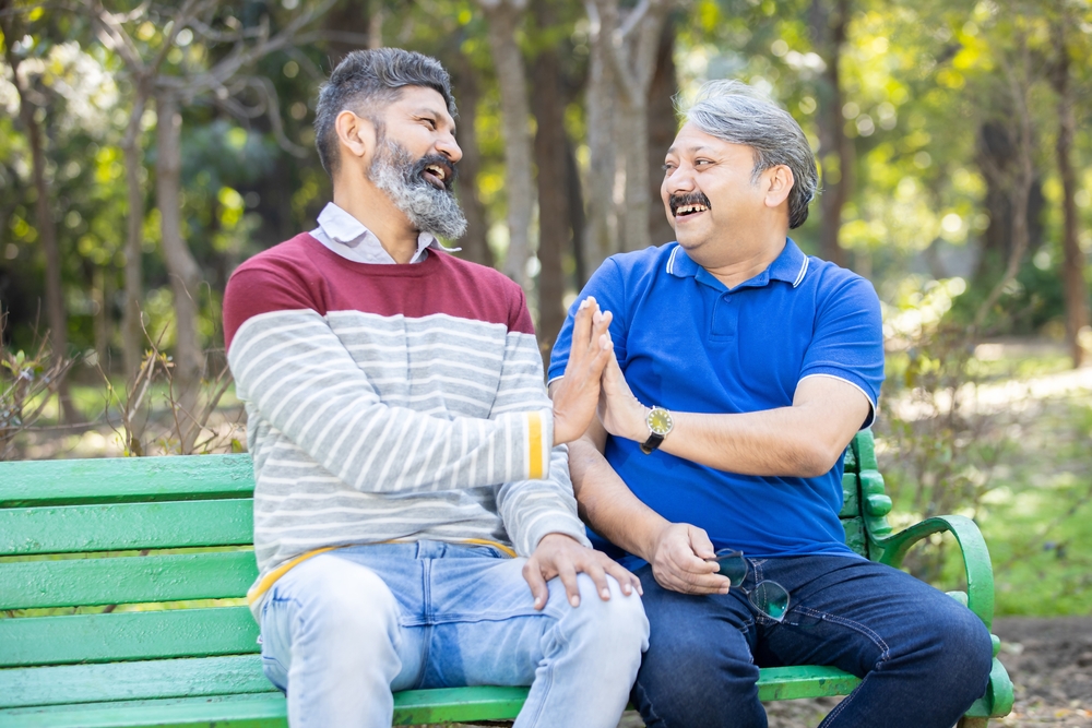 Two happy men sit on park bench exchanging a high five