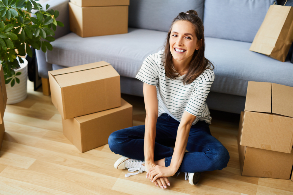 smiling caucasian woman sitting next to boxes in new apartment