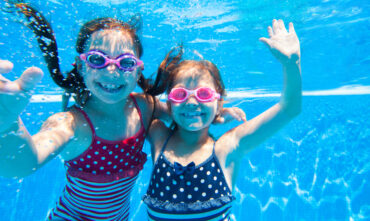 two young children underwater in pool with goggles on