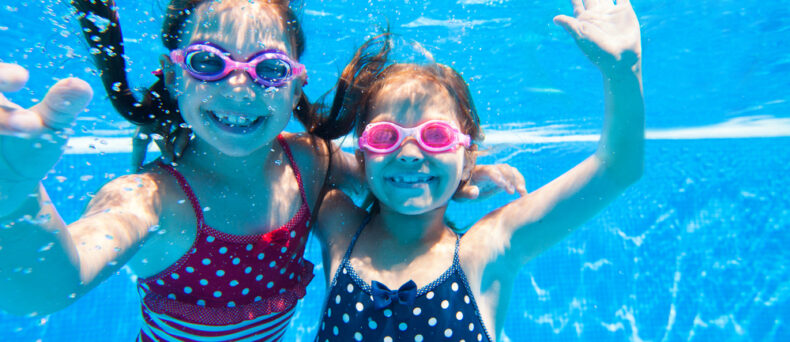 two young children underwater in pool with goggles on