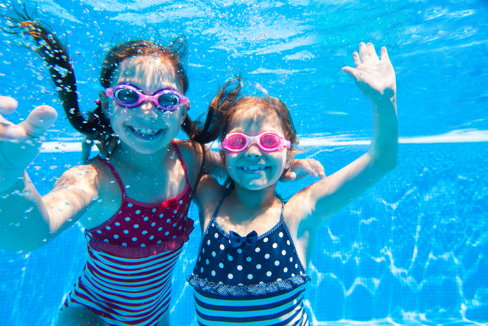 two young children underwater in pool with goggles on