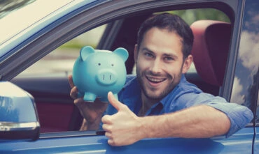 man in driver's seat of car smiling with piggy bank and thumbs up