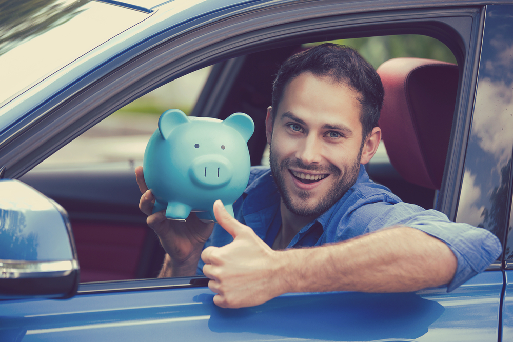 man in driver's seat of car smiling with piggy bank and thumbs up