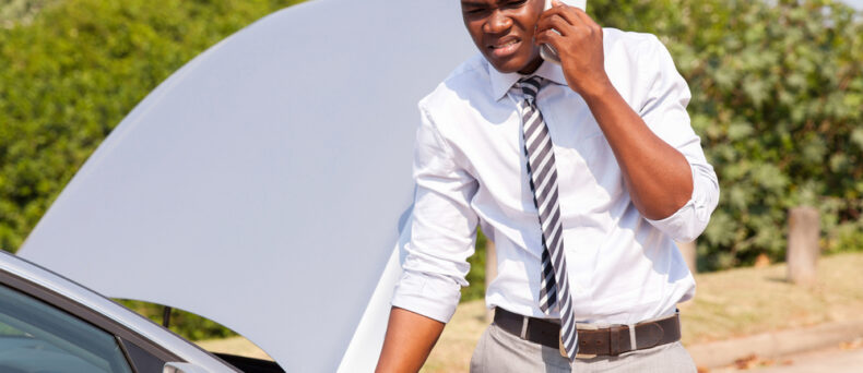 man on phone with roadside assistance in front of broken down car