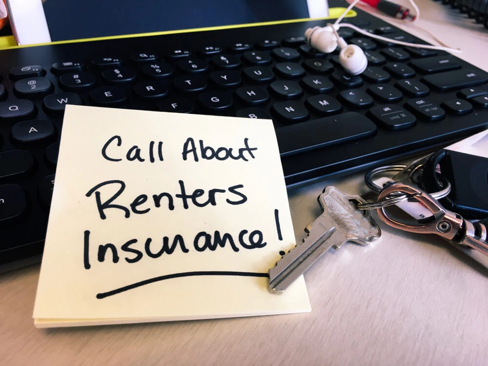 Sticky note reading ‘Call About Renters Insurance’ next to house keys on a desk, emphasizing the importance of securing renters insurance for personal property protection.