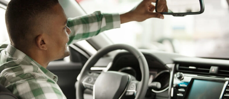 driver adjusting rear view mirror in car