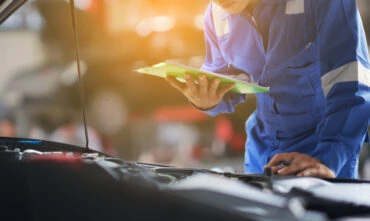 mechanic working on car with hood up and check list
