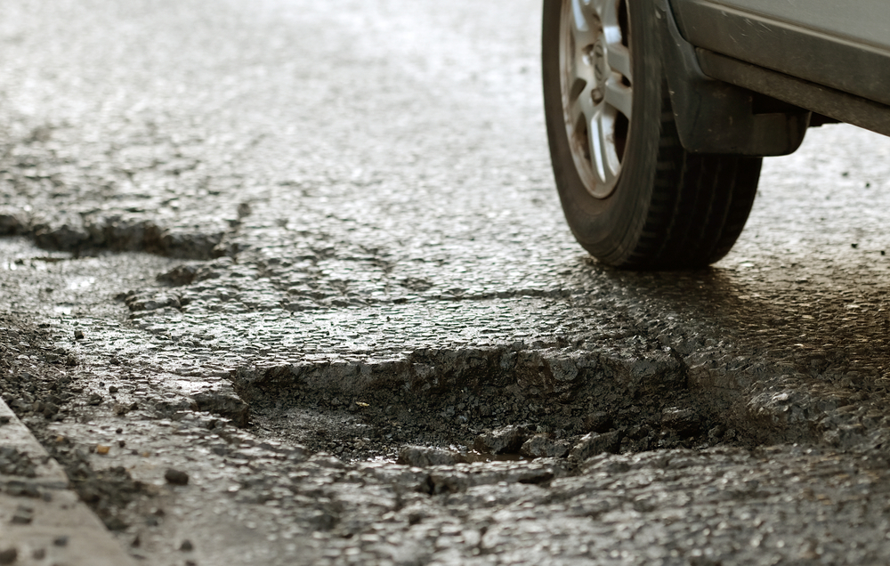 car driving on road with large pot hole