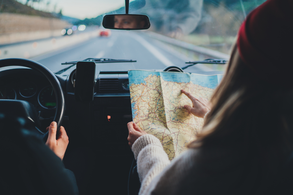 couple in car with woman in passenger seat looking at map