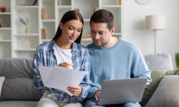 Couple reviewing documents and laptop at home while comparing options to switch car insurance and lower their monthly costs.