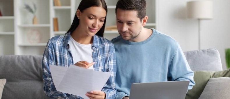 Couple reviewing documents and laptop at home while comparing options to switch car insurance and lower their monthly costs.