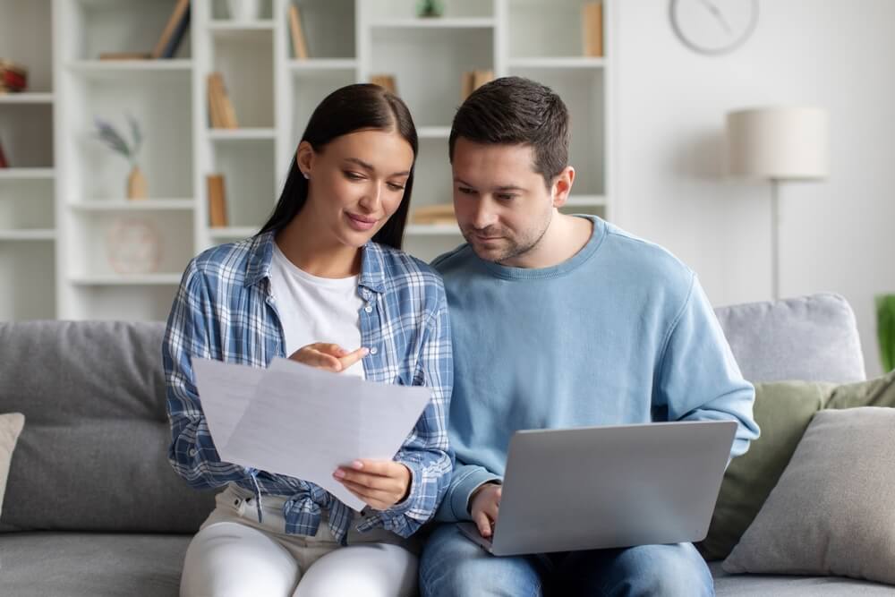 Couple reviewing documents and laptop at home while comparing options to switch car insurance and lower their monthly costs.