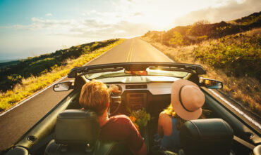 couple driving down road in convertible with the top down
