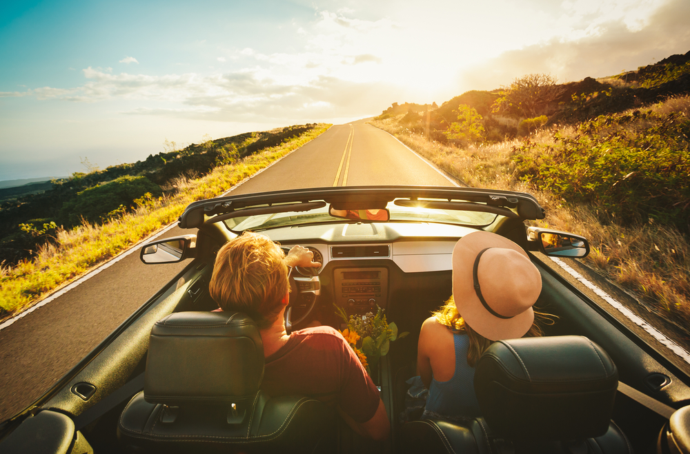 couple driving down road in convertible with the top down