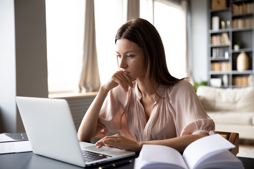 woman searching on laptop next to book