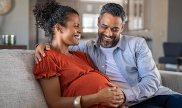 husband and pregnant wife sitting on couch smiling