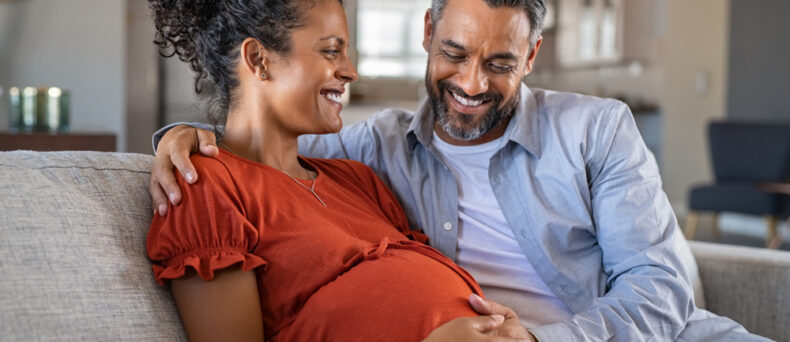 husband and pregnant wife sitting on couch smiling