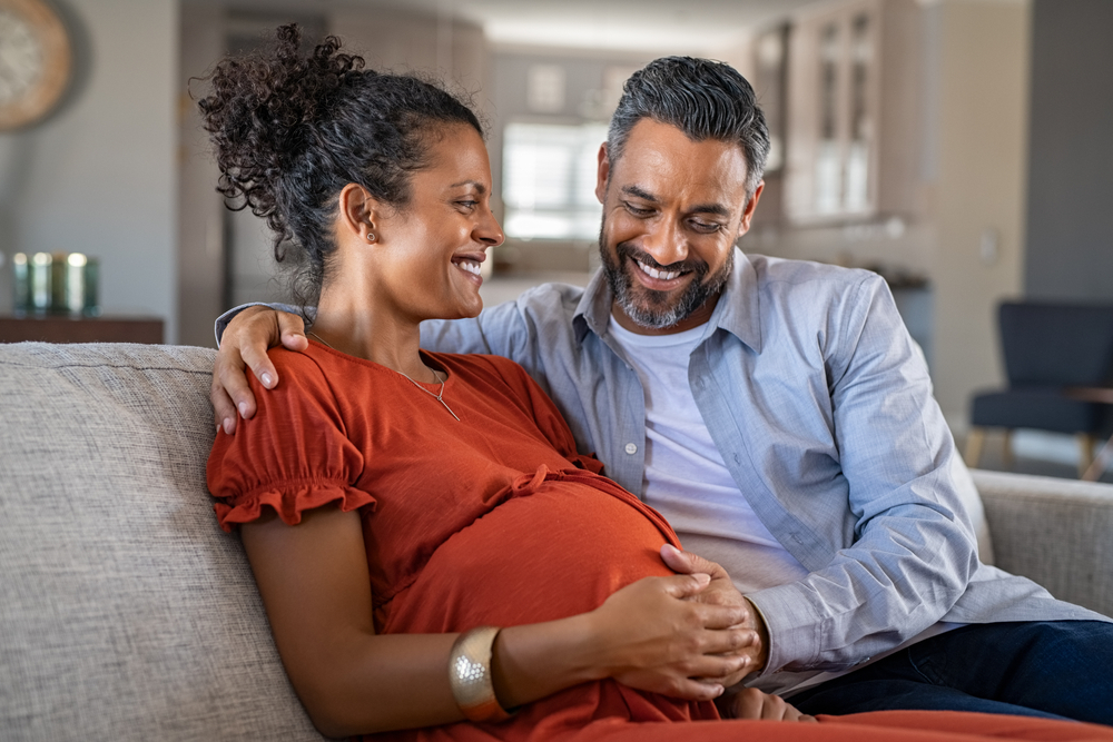 husband and pregnant wife sitting on couch smiling