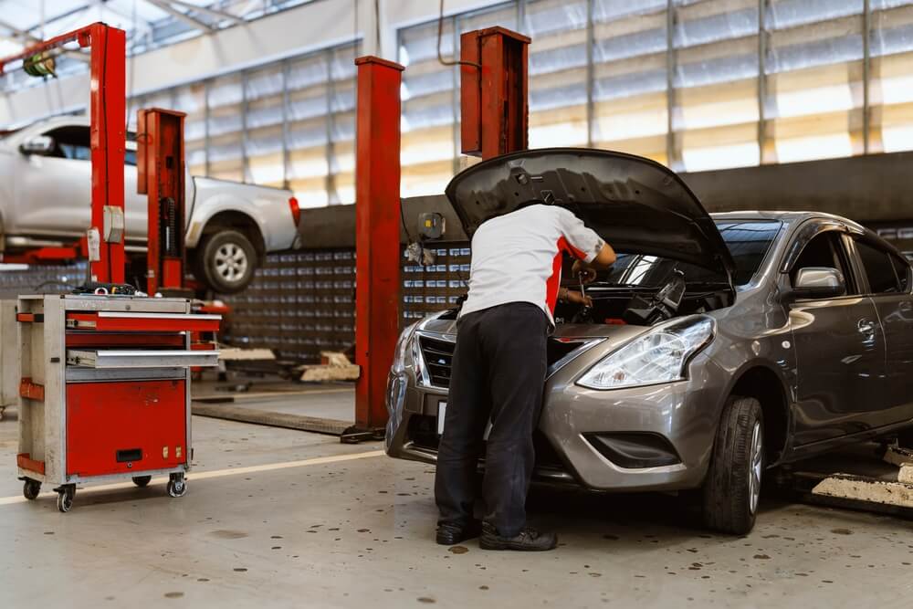 Auto technician working under a car hood, illustrating the importance of avoiding car repair scams with trusted service