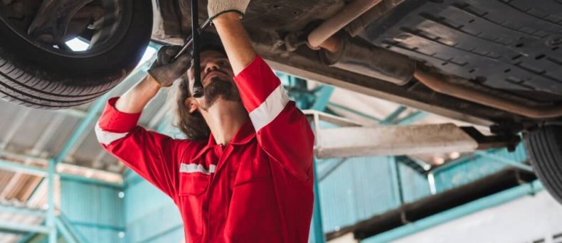 Mechanic inspecting a vehicle underside, highlighting how to spot common car repair scams before approving repairs.