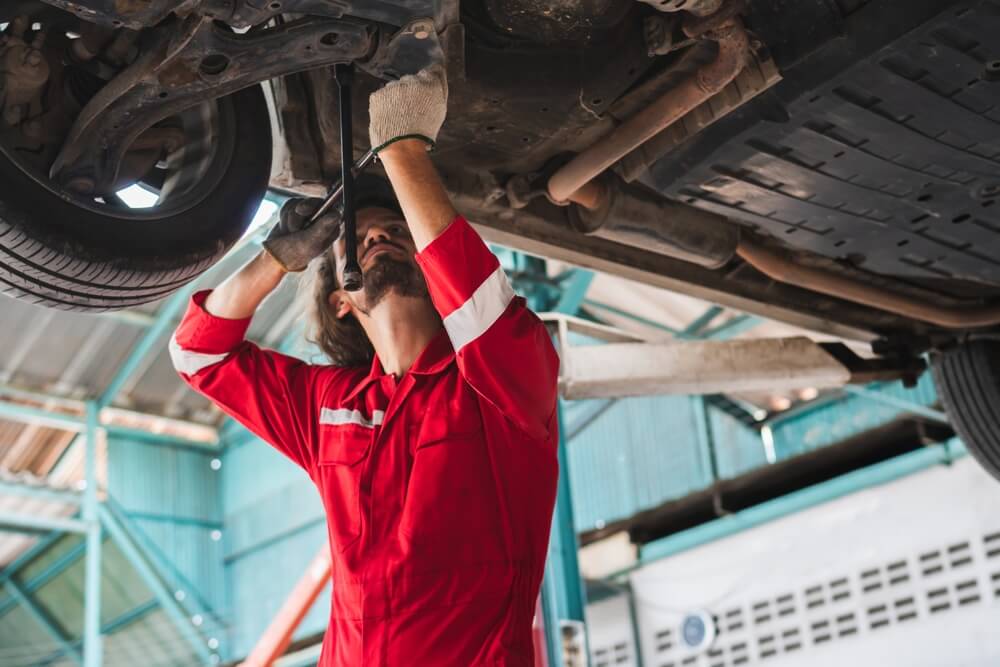 Mechanic inspecting a vehicle underside, highlighting how to spot common car repair scams before approving repairs.