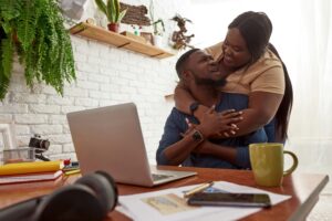 Young and happy black millennial couple who look at each other while searching for home insurance online. 