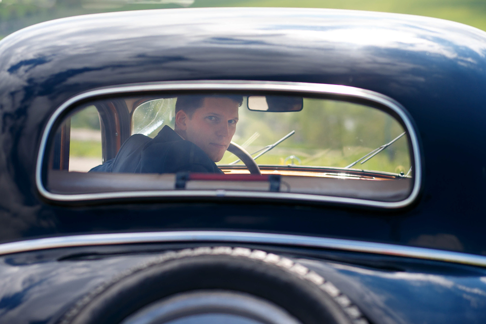 man looks back through the rear window of a classic car