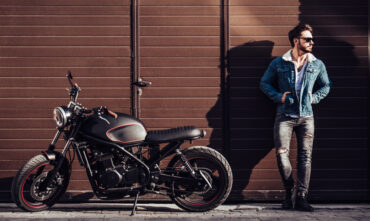 Handsome man stands against wall with his motorcycle parked next to him