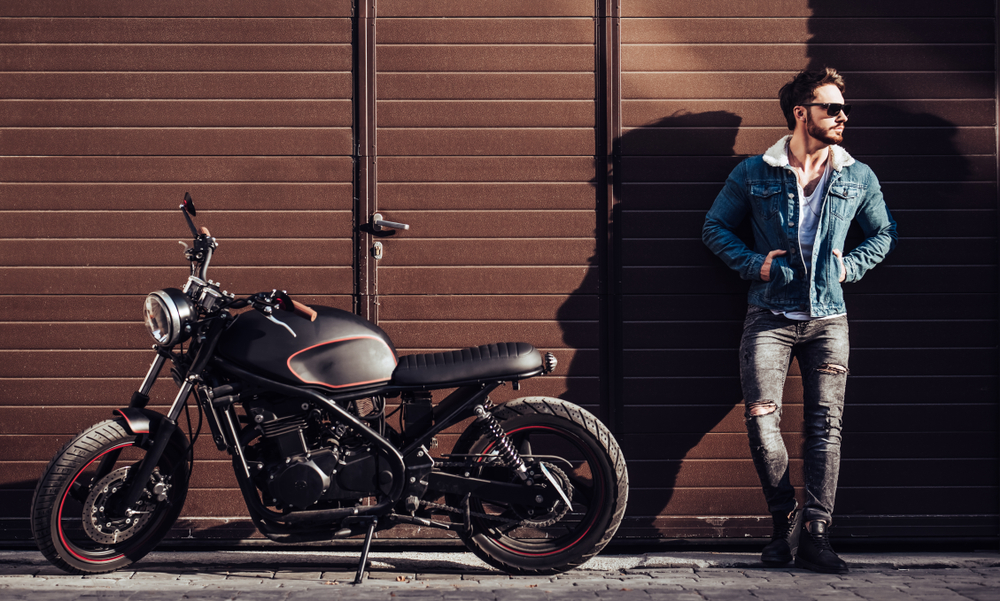 Handsome man stands against wall with his motorcycle parked next to him