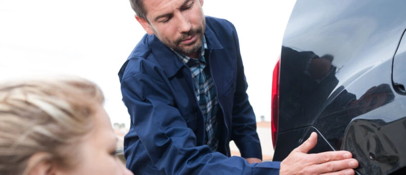 Man and woman examine a dent in a car