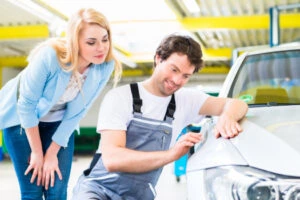 man works on dent in car while woman looks on