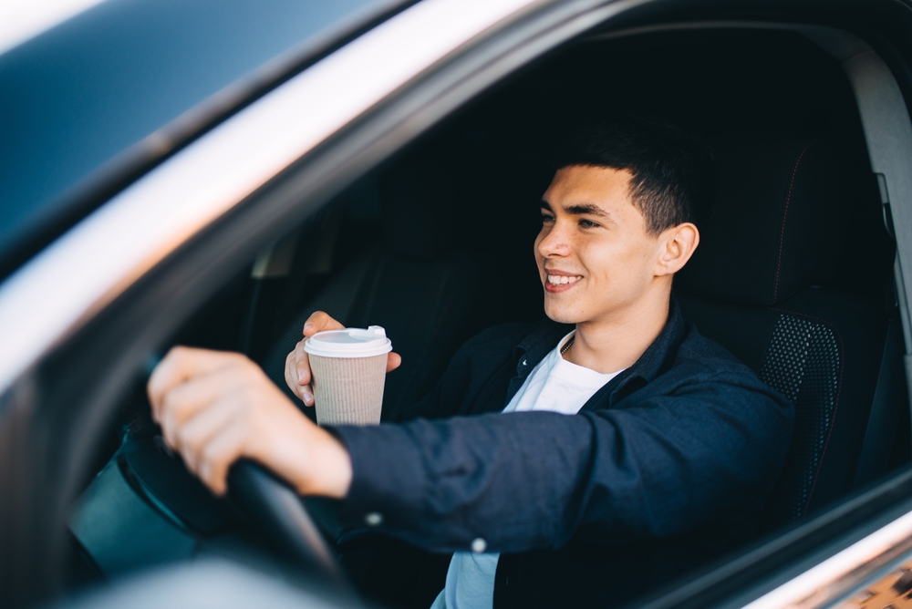smiling young man behind the wheel with coffee cup