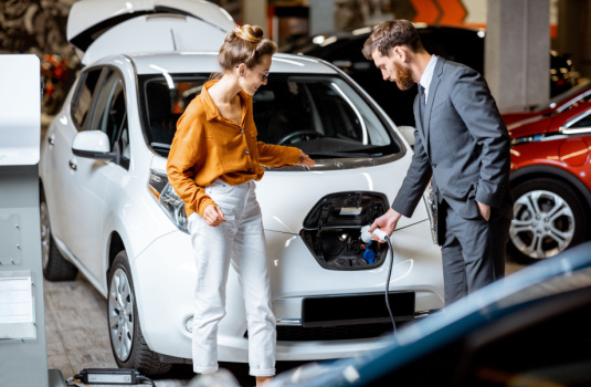 Car salesman showing young woman how to plug in an electric car in Georgia