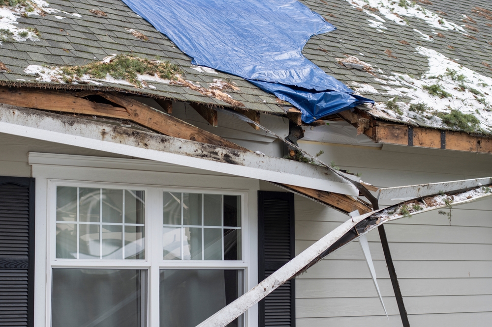 Home with severe roof damage covered by a blue tarp after a winter storm for a home insurance claim.