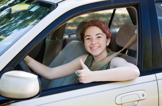 Young teen girl sits in drivers seat smiling